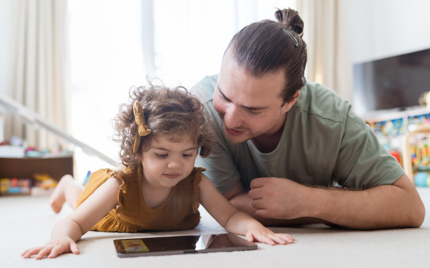 Father playing with his daughter on tablet in lounge